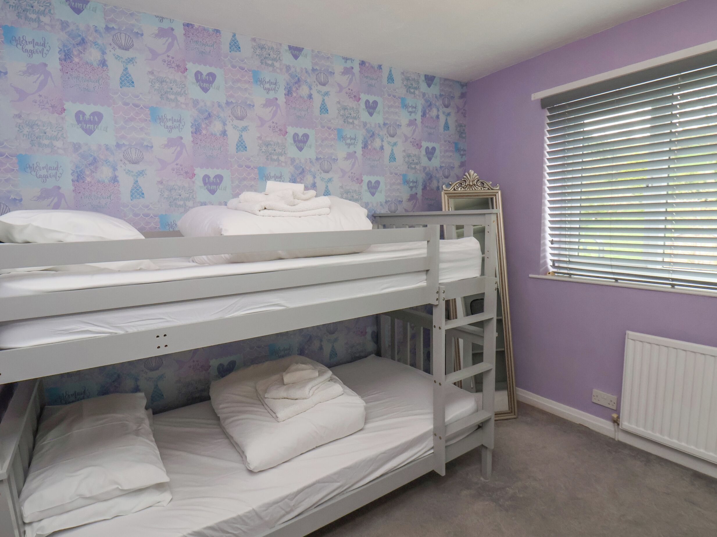 A bunk bed room with a purple wall and a window with blinds.