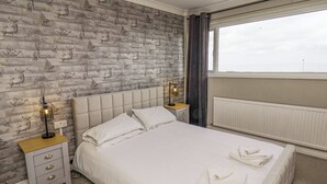 A bedroom with a large bed, two bedside tables, a nightstand, a window with curtains, and a wall with a nature-themed wallpaper. - 315 Filey Road (Scarborough)