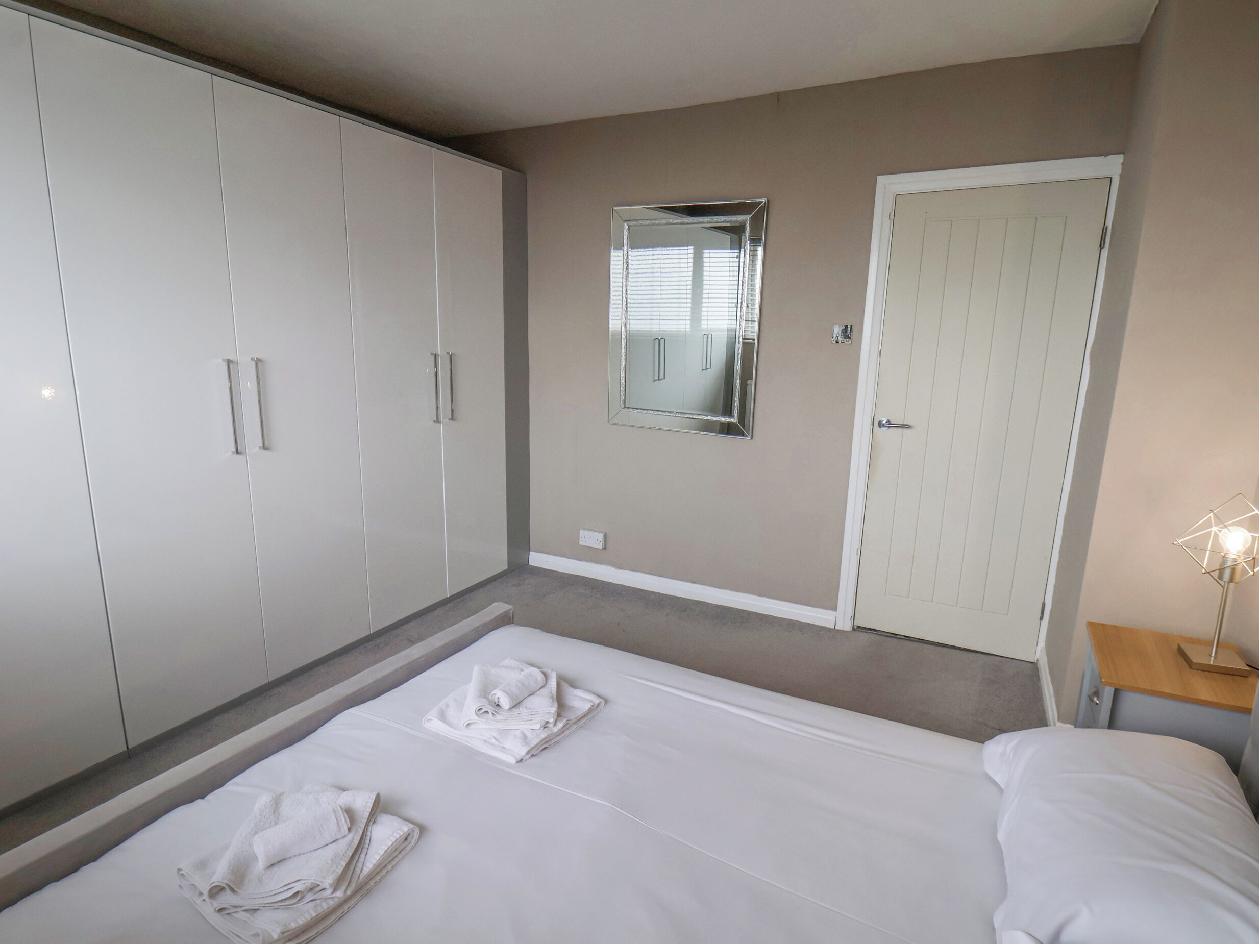 A hotel room with a bed, a wardrobe, a mirror, and a bedside lamp.