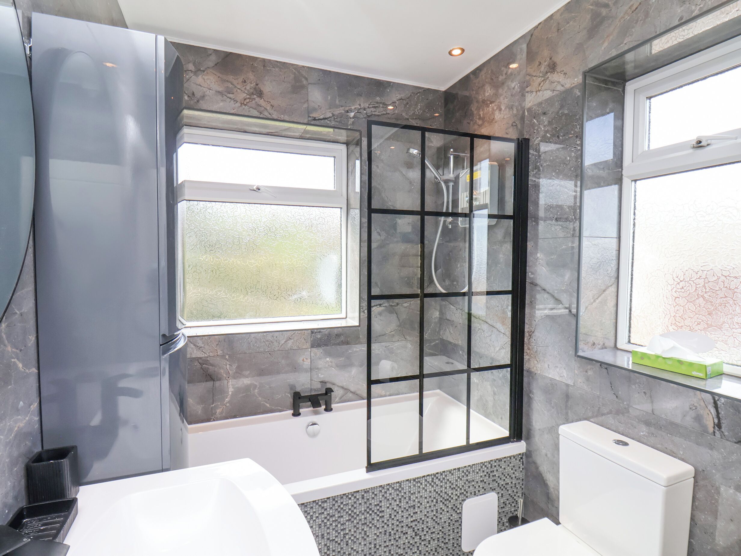 A modern bathroom with a glass-enclosed shower, a white bathtub, and a toilet.