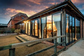 Una casa moderna con un porche de cristal, un granero de ladrillo y un patio de grava.