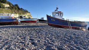 Boats docked on a pebbled beach with a cliff in the background. - Belfry Cottage (Colyton)