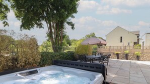 A hot tub with a stone wall and a patio area with outdoor furniture. - Ingleborough (Carnforth)