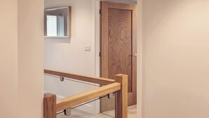A wooden staircase with a handrail, a door with a wooden panel, and a wall-mounted mirror. - Ingleborough (Carnforth)