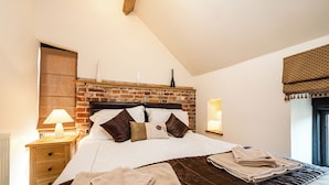 A neatly made bed with a brown quilt, a wooden nightstand with a lamp, and a brick-patterned headboard. - Snipe (Beccles)