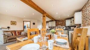 A cozy dining area with wooden furniture, a brick wall, and a kitchen in the background. - Snipe (Beccles)