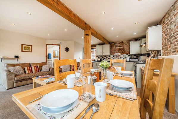 A cozy dining area with wooden furniture, a brick wall, and a kitchen in the background. - Snipe (Beccles)