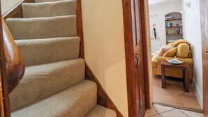A carpeted staircase with wooden handrails leading to a living room with a sofa and a small table. - Birch Cottage (Skipton)