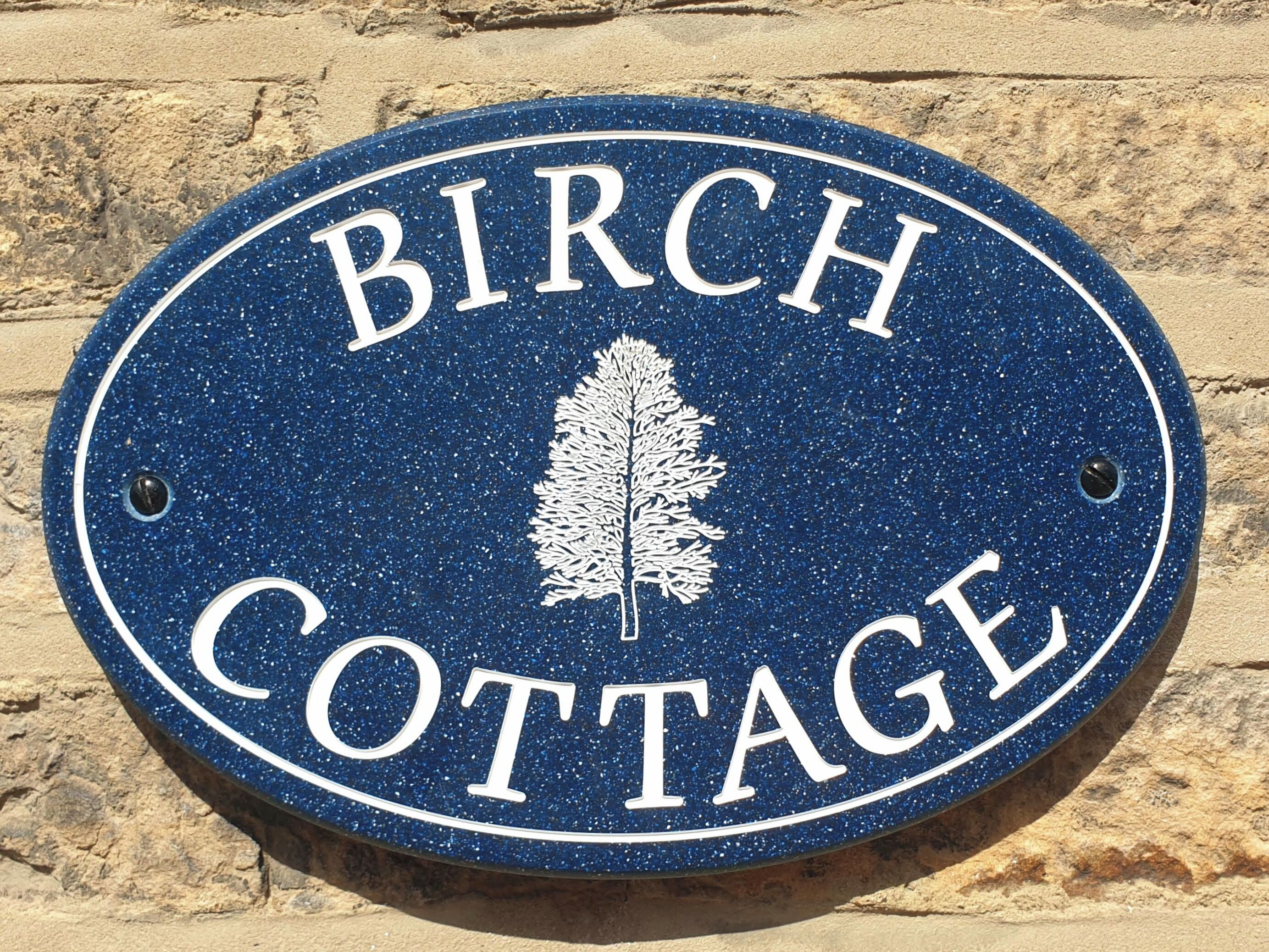 Une enseigne portant l’inscription « BIRCH COTTAGE » et représentant un arbre.