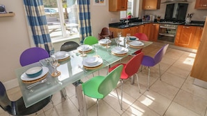 A dining area with a glass table set for six, surrounded by colorful chairs. - Archway House (Haverfordwest)