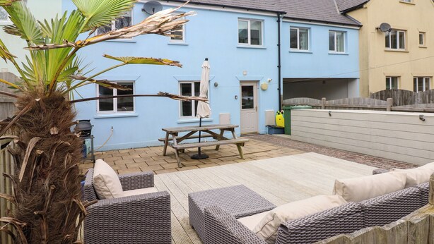 A patio with wicker furniture, a wooden table, and a bench. - Archway House (Haverfordwest)