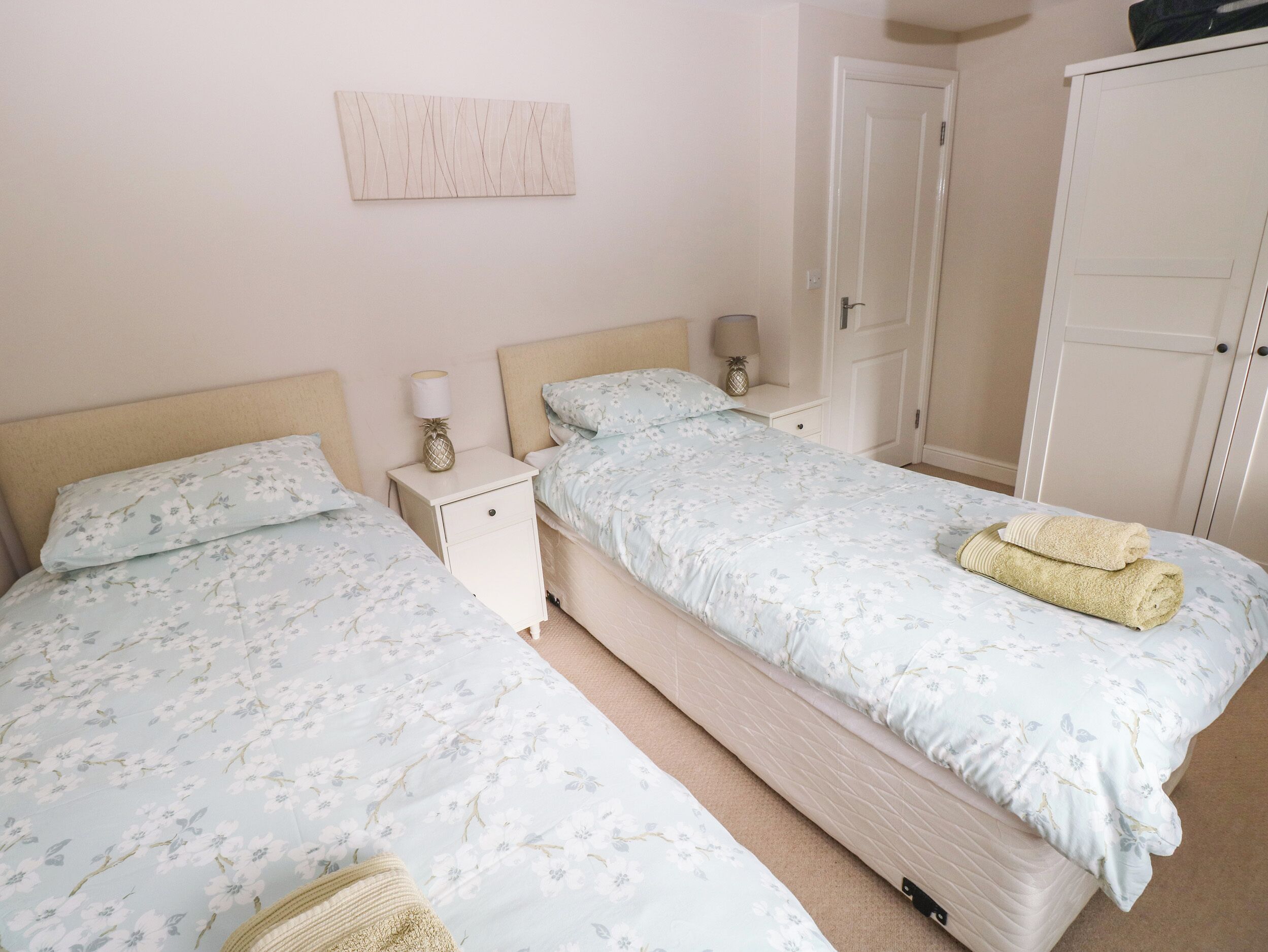 A bedroom with two beds, a nightstand with a lamp, and a wardrobe.