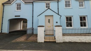 A light blue two-story house with a front door, a small porch, and a paved driveway. - Archway House (Haverfordwest)