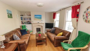 A living room with a brown leather sofa, a green armchair, a wooden coffee table, and a fireplace. - Archway House (Haverfordwest)