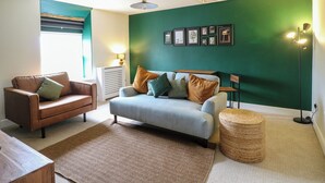 A living room with a brown leather sofa, a light blue sofa, a woven ottoman, and a green accent wall. - The Loft at The Old Dog Thorpe (Ashbourne)