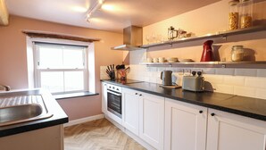 A kitchen with white cabinets, a black countertop, a window, and various kitchen appliances. - The Loft at The Old Dog Thorpe (Ashbourne)