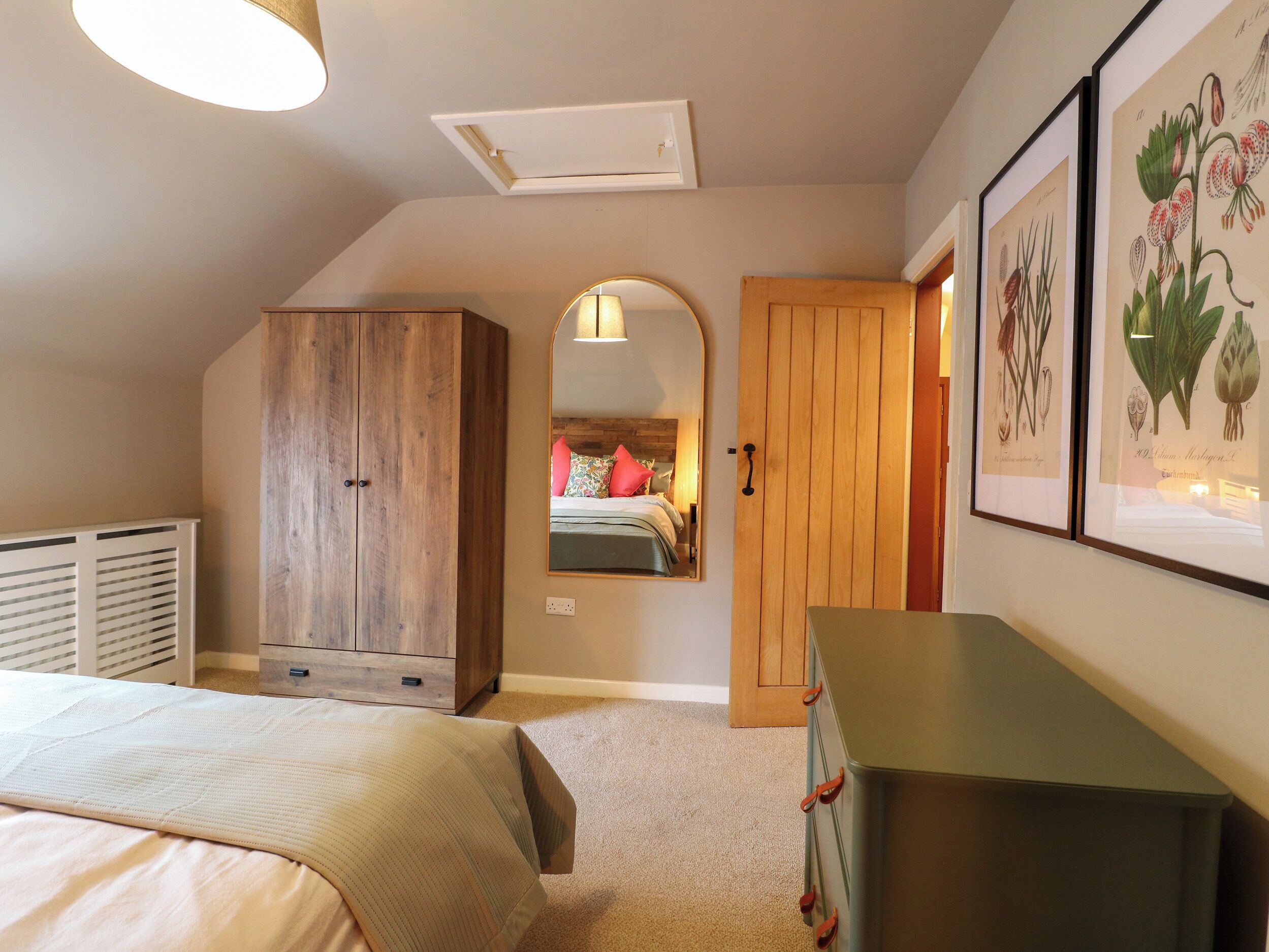 A bedroom with a bed, wardrobe, dresser, and framed botanical prints.