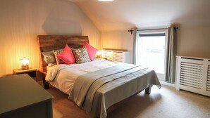 A bedroom with a wooden headboard, a bed with multiple pillows, a bedside table with a lamp, and a radiator. - The Loft at The Old Dog Thorpe (Ashbourne)