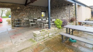 A covered outdoor seating area with stone walls, tables, and chairs. - The Loft at The Old Dog Thorpe (Ashbourne)