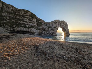 Un paysage côtier caractérisé par une arche rocheuse naturelle, une plage de sable et l’océan.