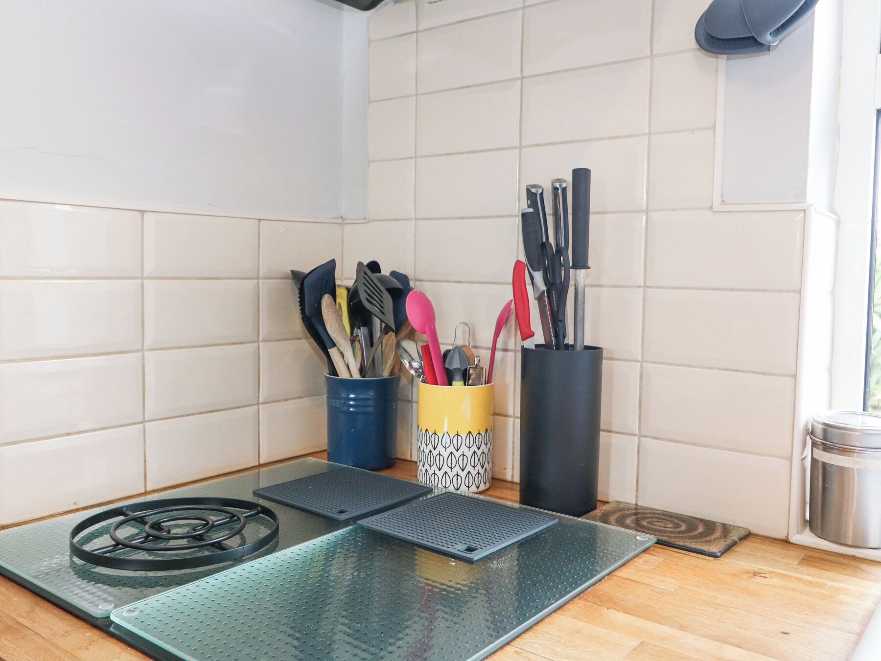 A kitchen with a gas stove, a glass mat, and utensils in holders.