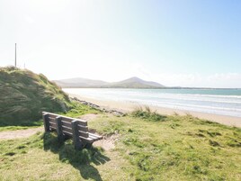 A bench on a grassy area overlooking a beach with a mountain in the background.