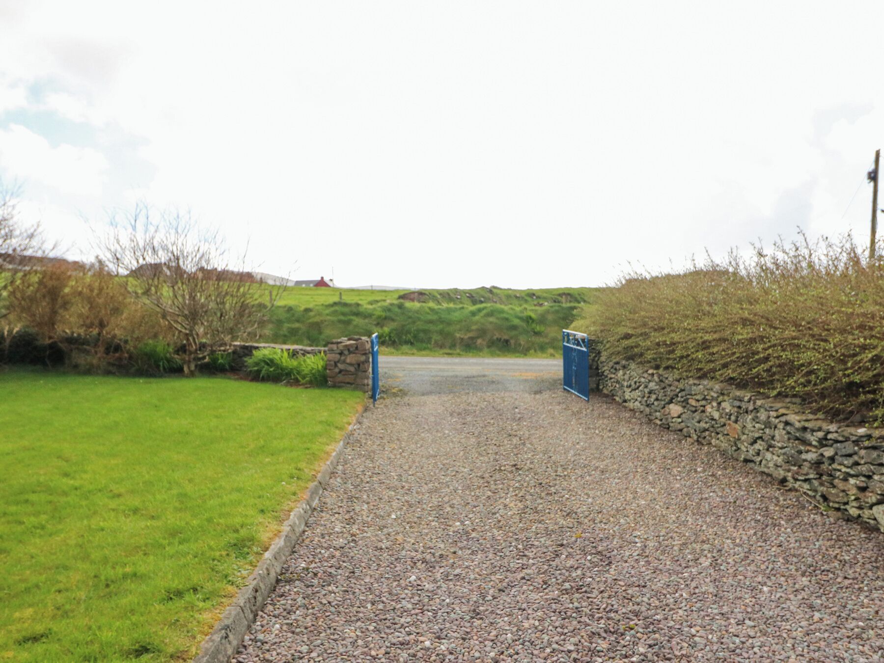 A gravel pathway leading to a stone wall and a blue gate.