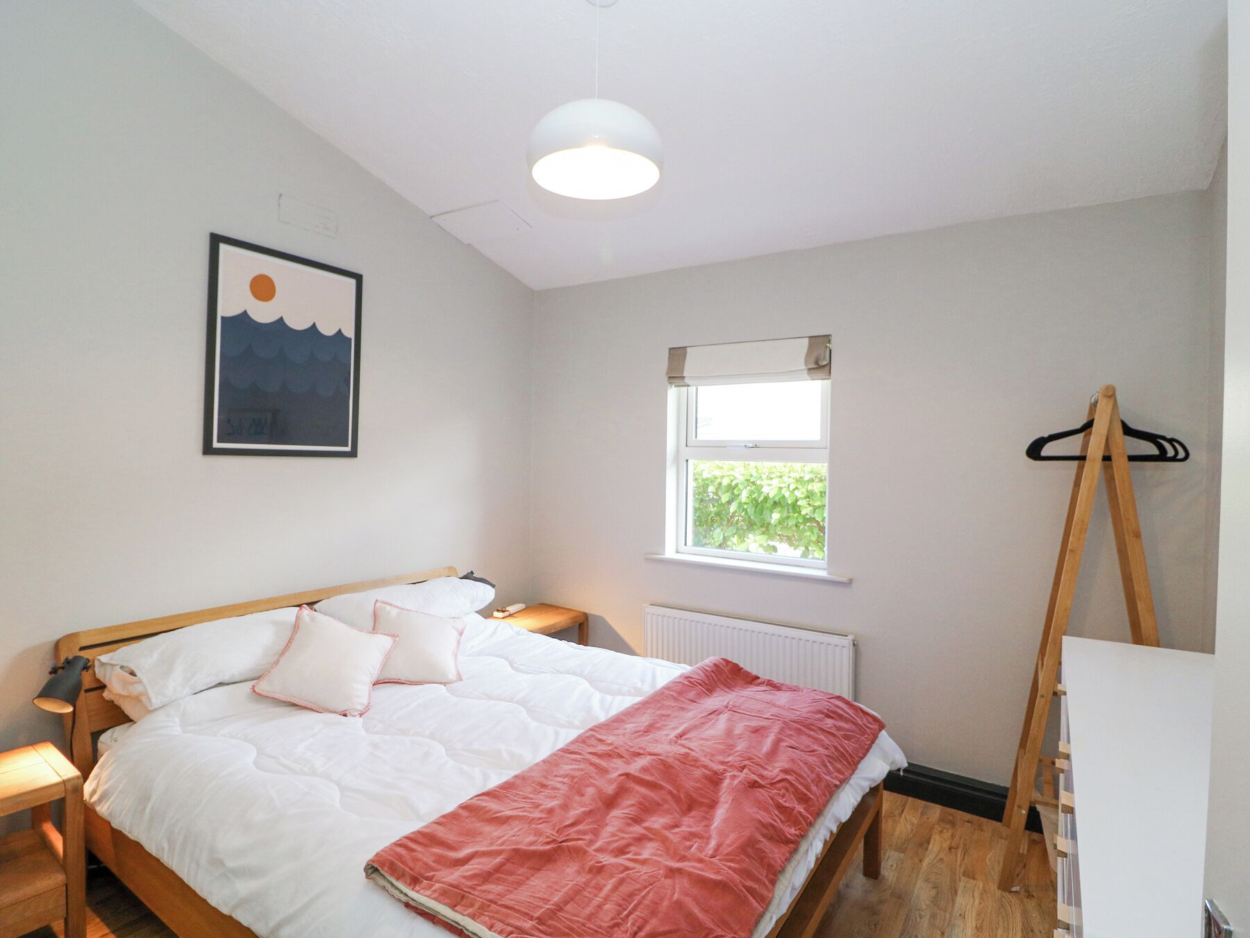 A bedroom with a bed, a bedside table, a window, a radiator, and a wooden easel.