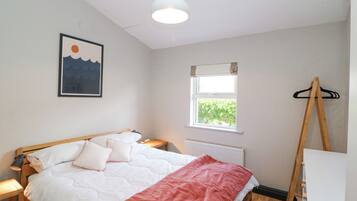 A bedroom with a bed, a bedside table, a window, a radiator, and a wooden easel.