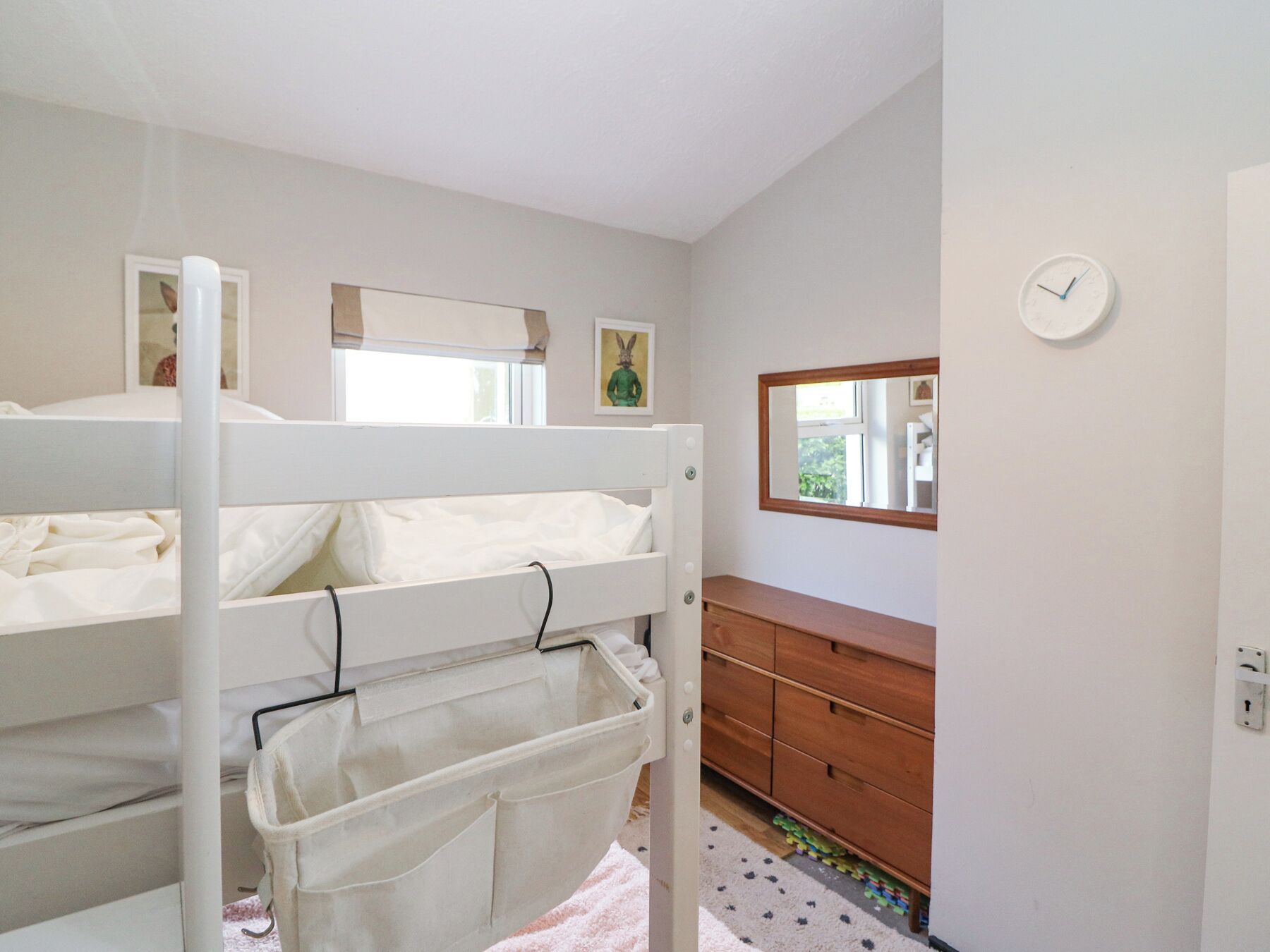 Un dormitorio con literas, un aparador, un espejo y un reloj en la pared.