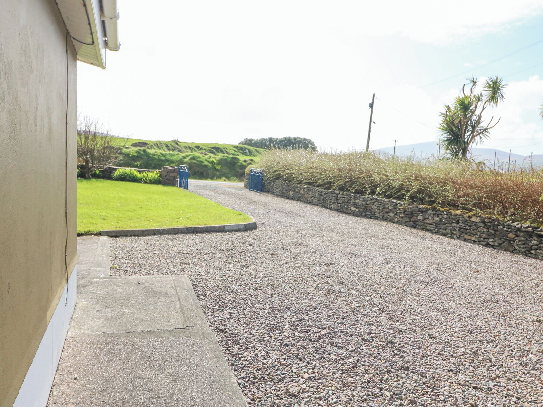 A gravel driveway leading to a house with a stone wall and a grassy area.