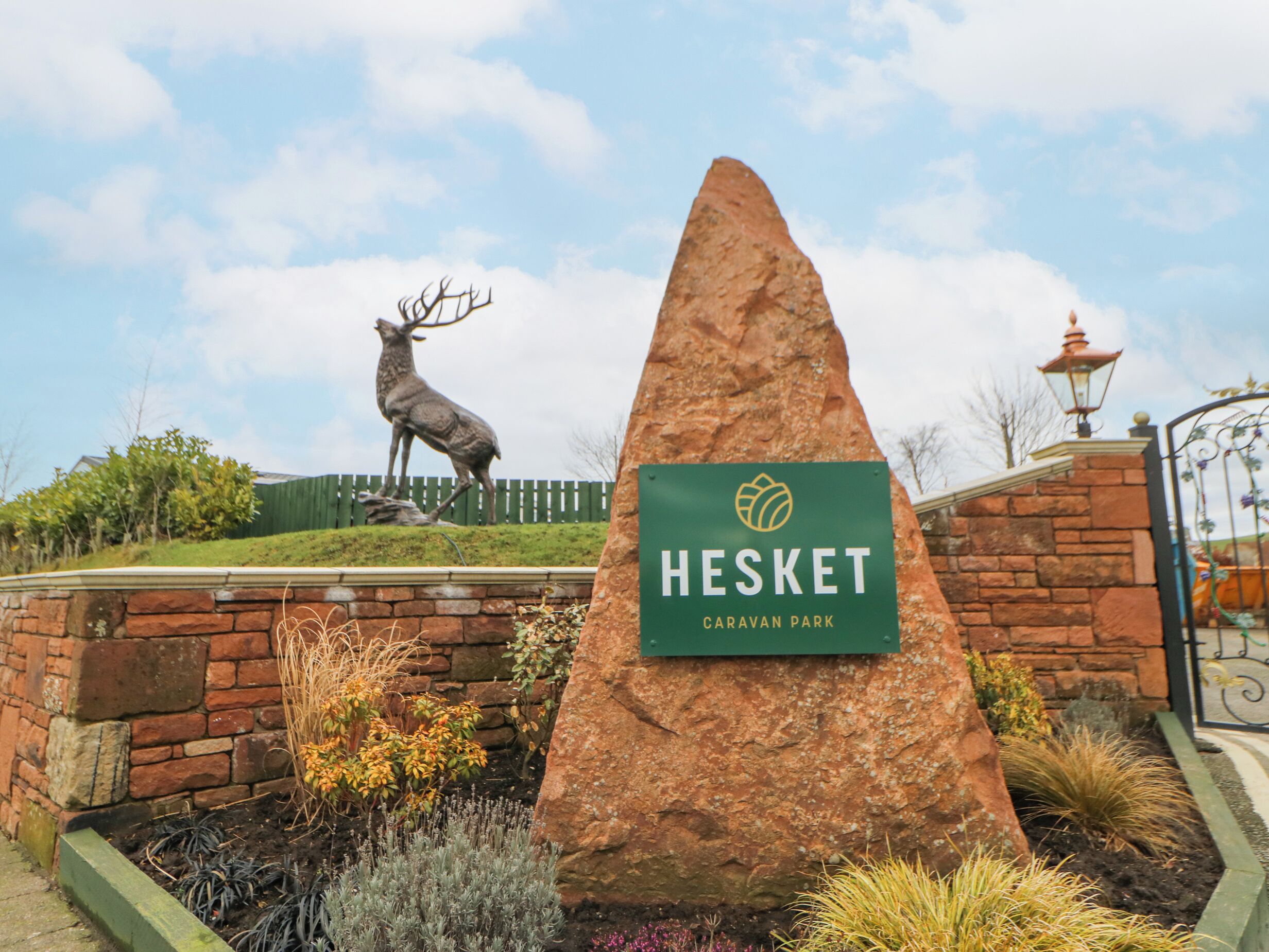 A sign for Hesket Caravan Park with a deer statue and landscaped garden.