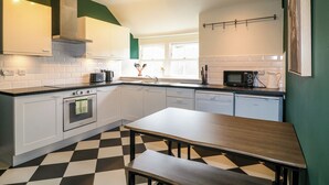 A modern kitchen with white cabinets, a black and white checkered floor, a wooden table, and a window with a view. - Apartment at The Old Dog, Thorpe (Ashbourne)