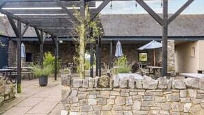 An outdoor patio area with stone walls, wooden pergola, and tables with umbrellas. - Apartment at The Old Dog, Thorpe (Ashbourne)