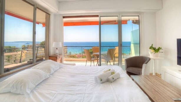 A hotel room with a bed, a bedside table, a chair, and a view of the sea.