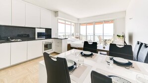 A modern hotel room with a kitchen, dining area, and a balcony with a view.