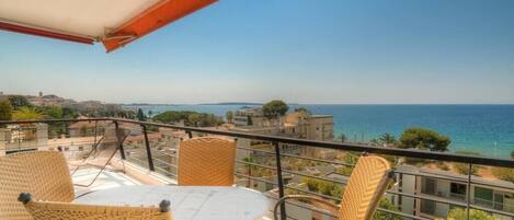 Un balcon avec des fauteuils et une table en osier, offrant une vue sur le paysage urbain de la côte.