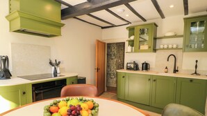 Una cocina con armarios verdes, una mesa redonda con un frutero, un tostador y una tetera.