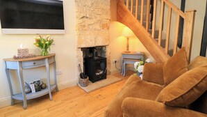 Una sala de estar acogedora con una chimenea de piedra, una escalera de madera y un sofá marrón confortable.