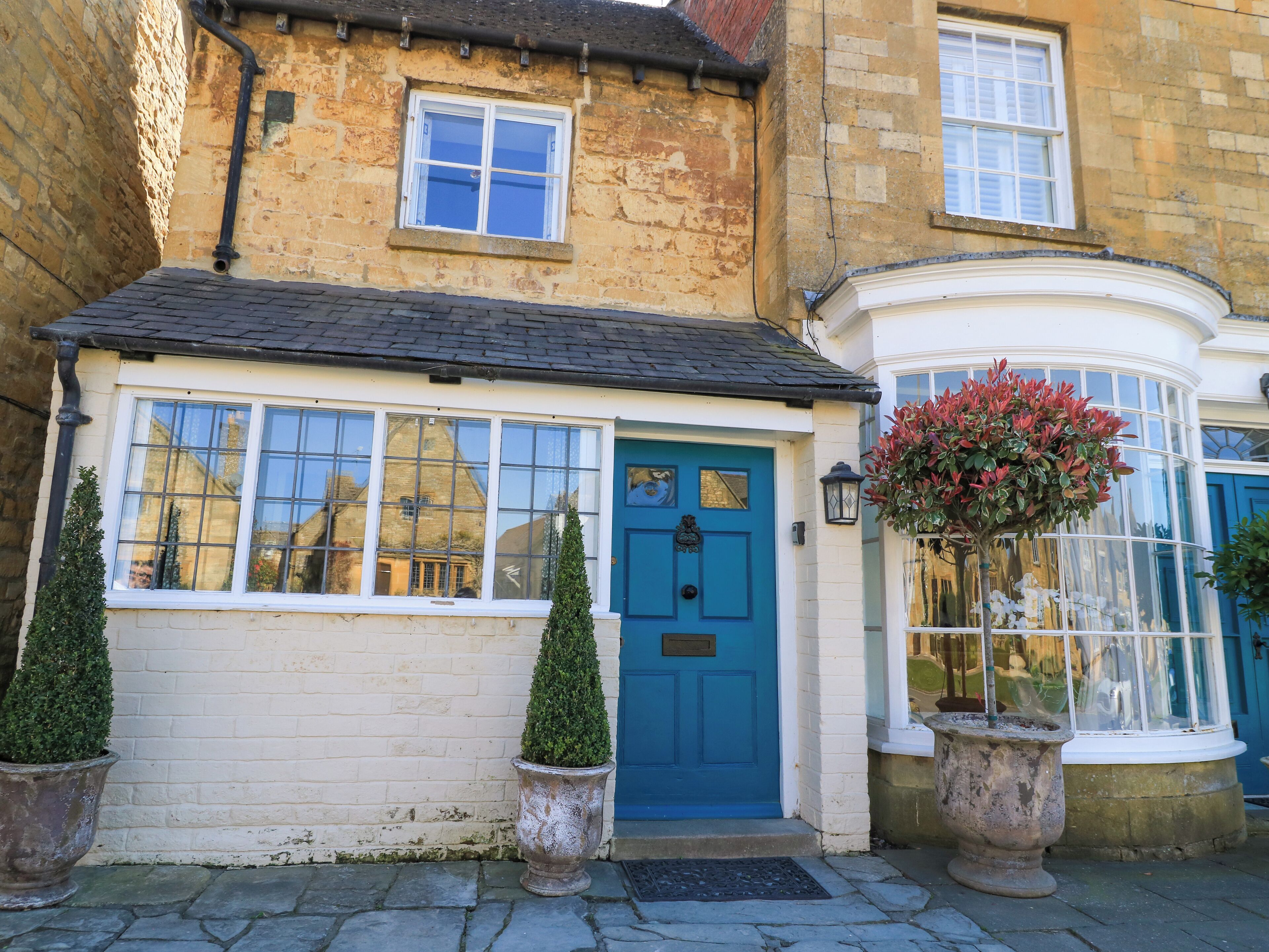 A traditional building with a blue door, large windows, and a small garden with potted plants.