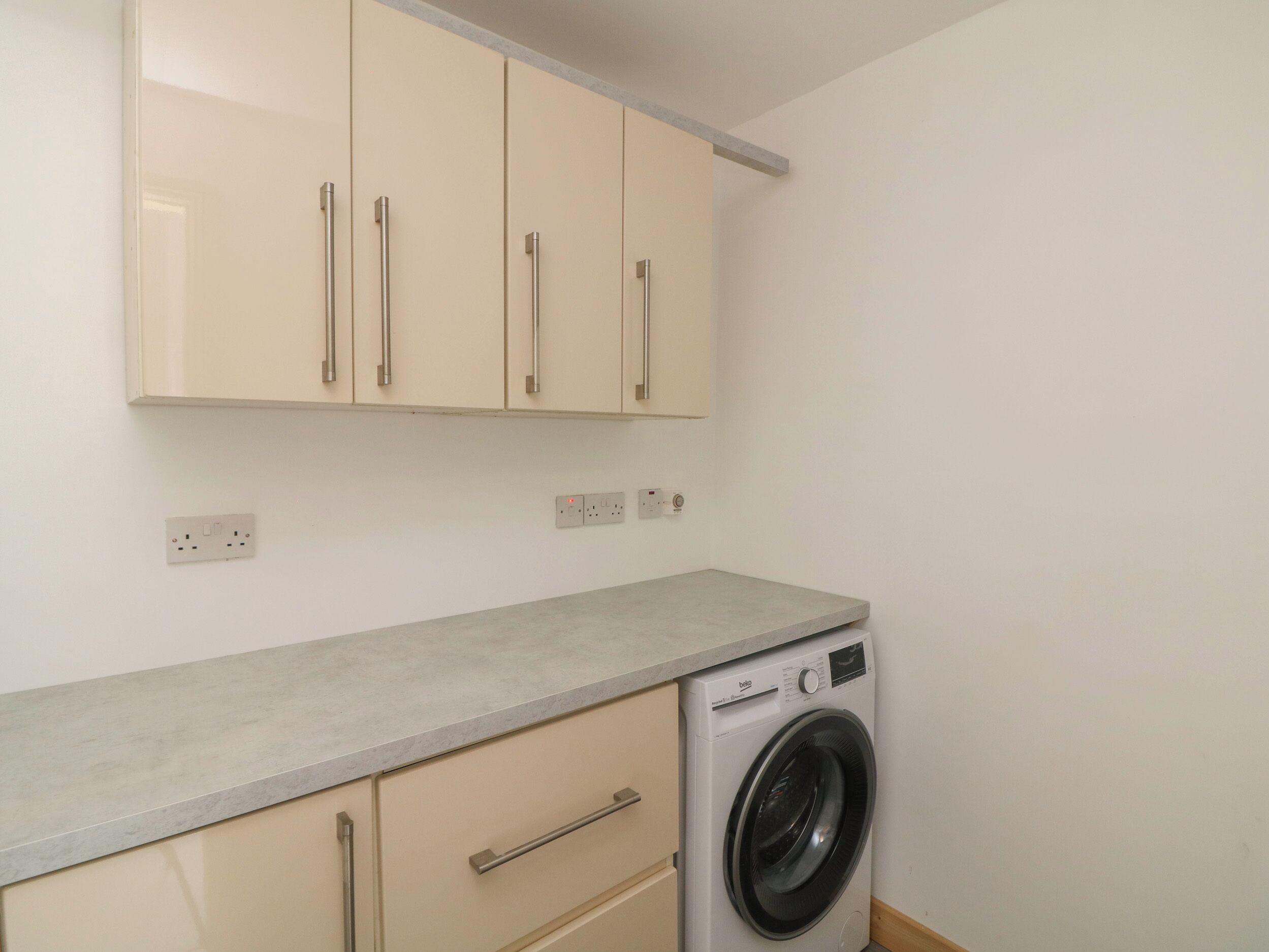 A compact laundry room with a washing machine, beige cabinets, and a countertop.
