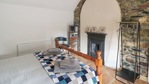 Une chambre avec un lit en bois, une couverture à carreaux, un mur en pierre et une cheminée.