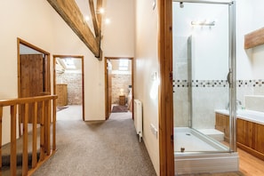 Een gang die uitkomt bij een badkamer met een glazen douchecabine, houten vloeren en een stenen muur op de achtergrond.