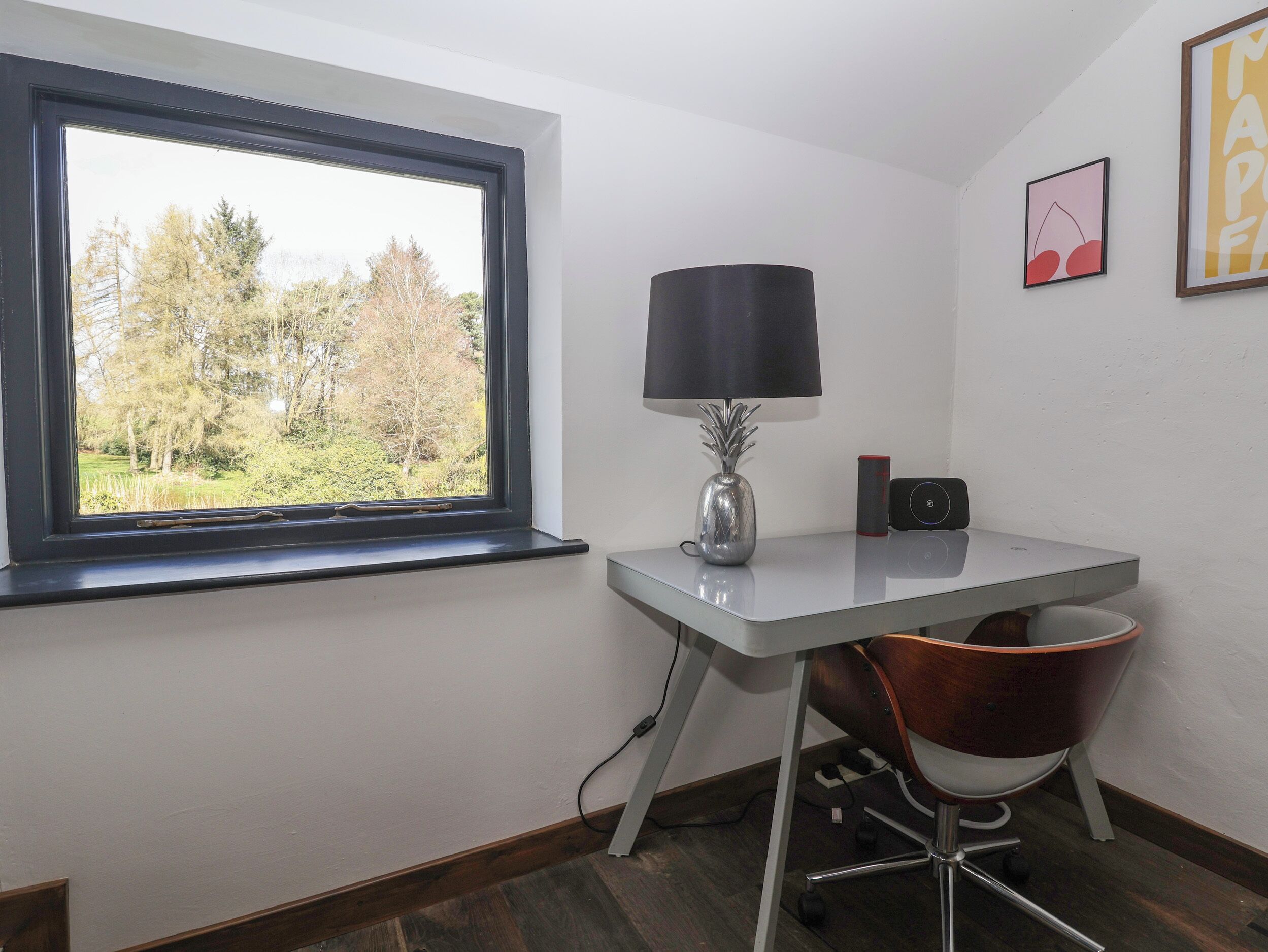A corner office with a desk, chair, lamp, and a view of trees through a window.