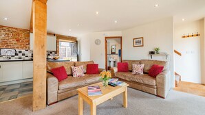 A modern living room with two leather sofas, a wooden coffee table, and a kitchen area with a brick wall and white cabinets. - Woodcock (Beccles)