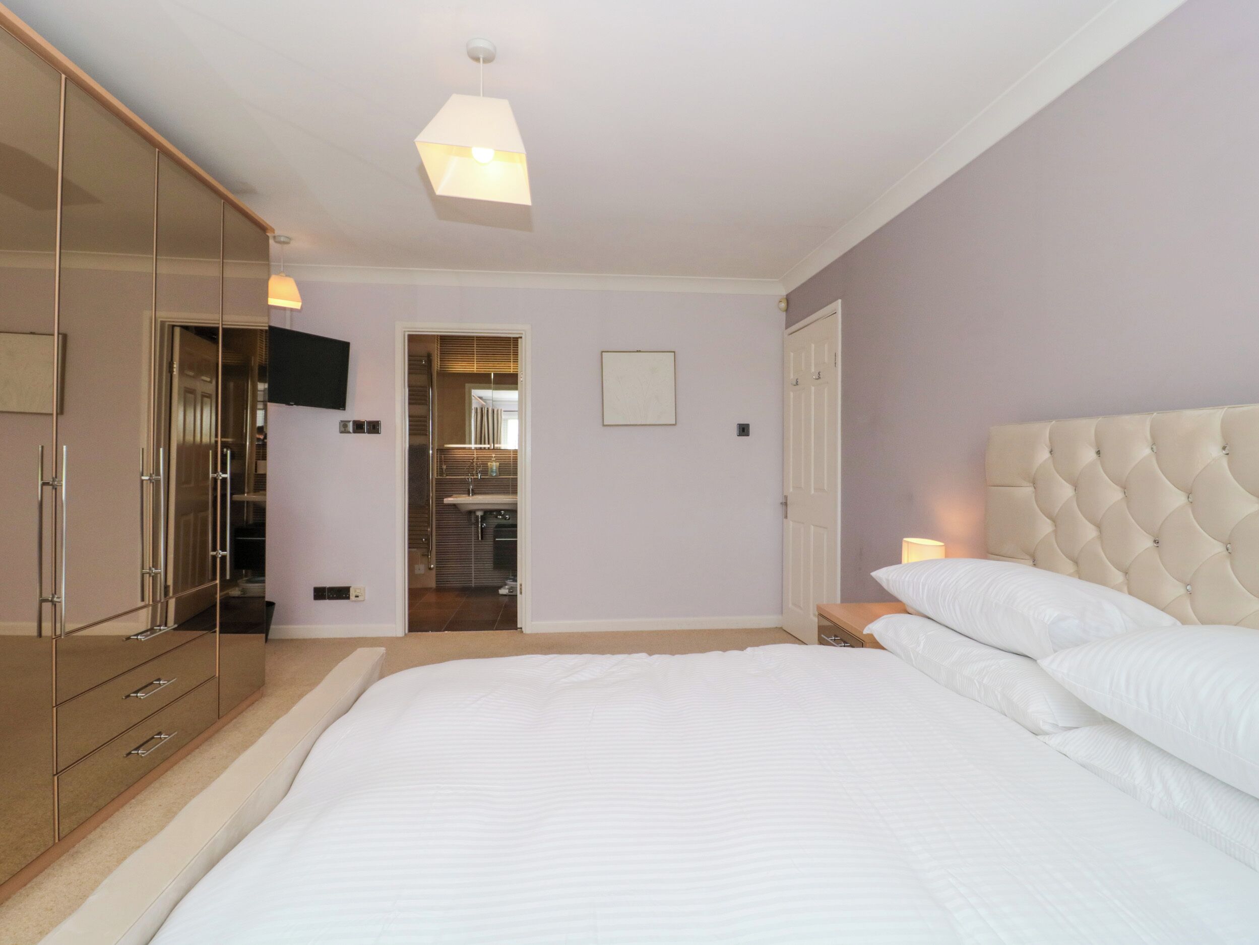 A bedroom with a large bed, a wardrobe, a television, and a bathroom visible through an open door.
