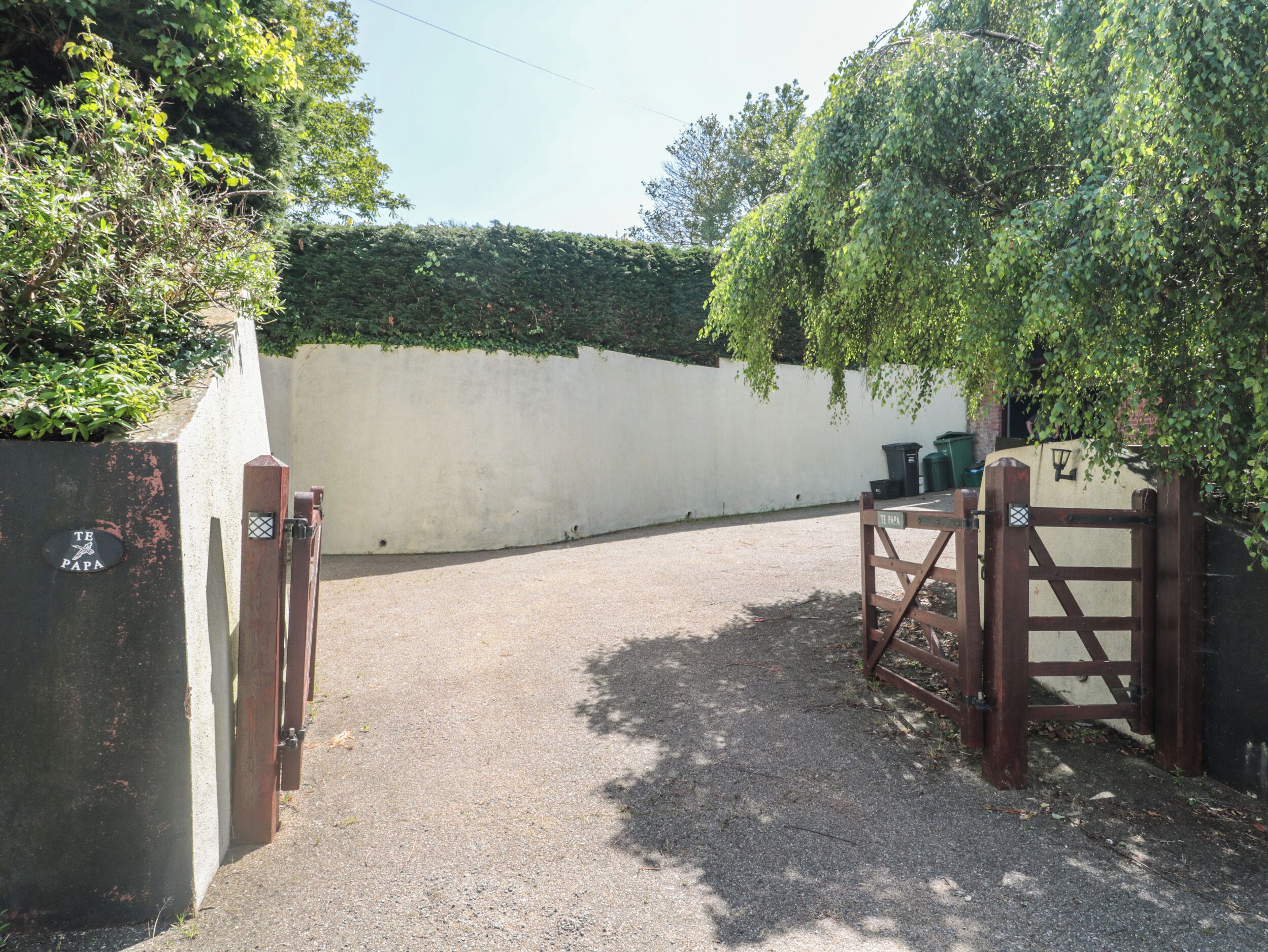 A gated driveway leading to a building with a white wall and a sign reading "TE PAPA".