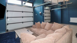 Et værelse med en stor sofa, et fjernsyn ophængt på væggen og et vindue med persienner.