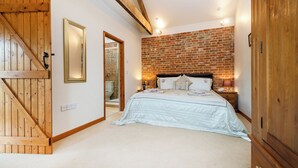 A bedroom with a brick wall, a bed with a white duvet, a wooden door, and a mirror. - Partridge (Beccles)