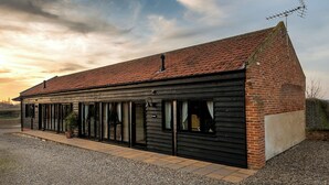 A long, narrow building with a sloped roof, large windows, and a chimney. - Partridge (Beccles)